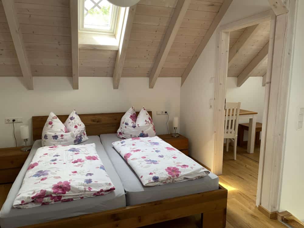 Das Doppelbett im offenen Schlafzimmer im OG des Ferienhauses mit geöffneter Tür zum Einzelzimmer